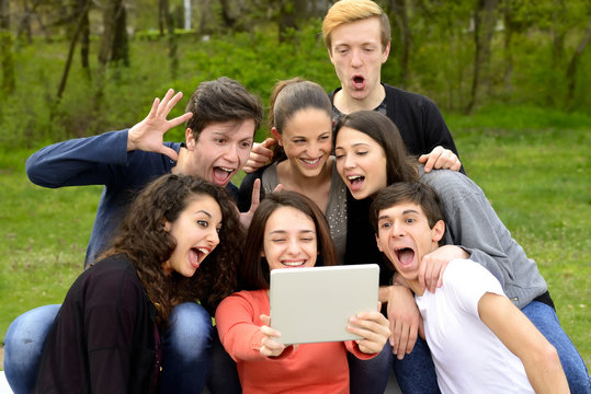 Group of friends having fun while using a tablet in a park