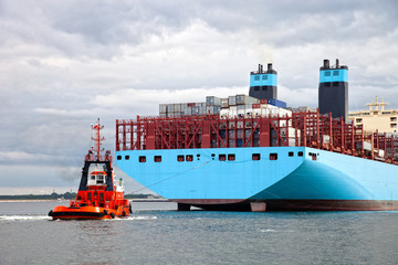 Container ship arriving at port, assisted by tugboat.