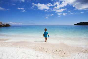 LIttle boy walking towards the water, looking at horizon.