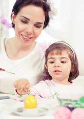 Obraz na płótnie Canvas Cute little girl painting Eater eggs with her mommy
