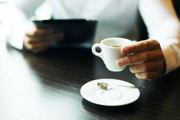 Cup of Coffee in hand. Blurred tablet computer in another