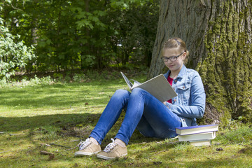 Young girl reading book in park in spring day