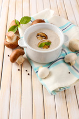 Mushroom soup in white pot, on napkin, on wooden background