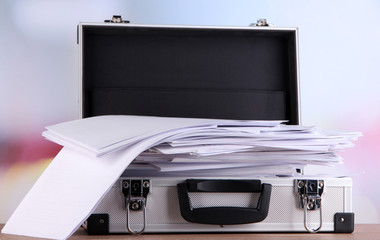 Briefcase full of papers, on wooden table, on light background