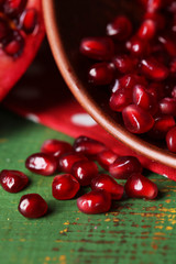 Ripe pomegranate seeds in bowl on color wooden background