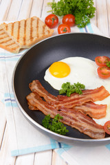 Scrambled eggs and bacon on frying pan on table close-up