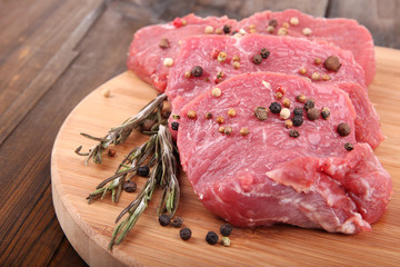 Raw beef meat with spices on cutting board on wooden background