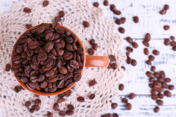 Cup full of coffee beans on light wooden background