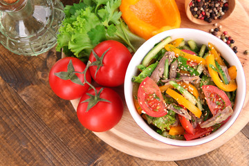 Beef salad in bowl with vegetables and spices on wooden table