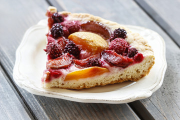 Piece of blueberry, peach and plum cake on rustic wooden table