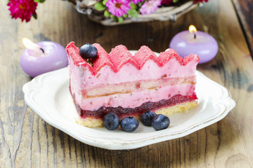 Pink layer cake decorated with fresh fruits on wooden table