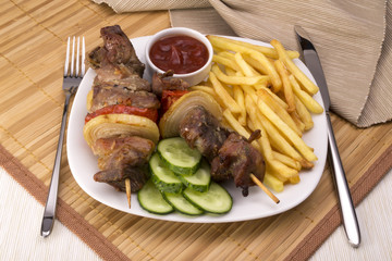 Kebab and fries, sauce, cucumber and fork knife