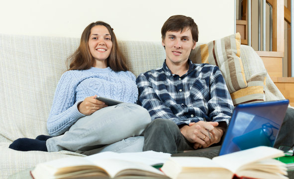 Two students with books and laptop sitting on the sofa