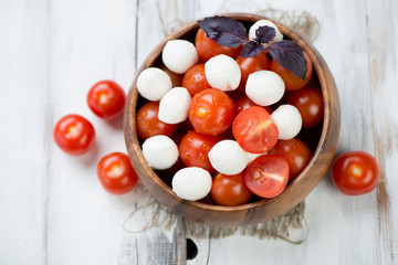 Wooden bowl with mozzarella and cherry tomatoes, view from above