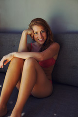 Pretty young female model in bikini sitting on a couch