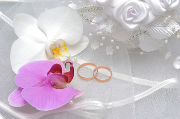 Wedding rings with orchid flowers and bridal veil on gray