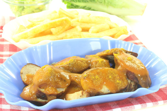 Currywurst mit Pommes Frites auf einer karierten Serviette