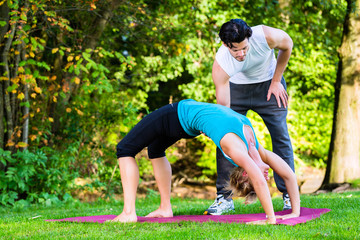 Junge Frau macht Joga  mit Trainer im Freien