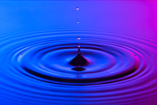 Water drop close up with concentric ripples colourful blue and p