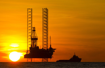 Offshore drilling rig and supply vessel at sunset