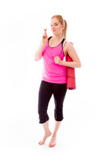 Young woman carrying exercising mat wishing with crossing finger