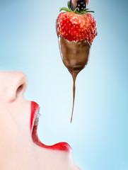 Fototapeta premium Seduction - red female lips eating chocolate strawberries