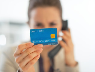 Closeup on business woman with credit card talking phone in offi