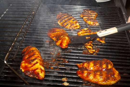 A spatula flipping barbecue chicken breasts cooking on a grill.