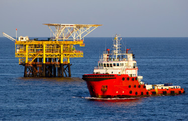 Offshore drilling rig and supply vessel at sunset