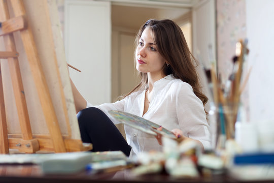 Long-haired woman paints picture on canvas
