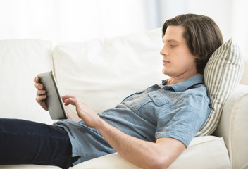 Man Using Digital Tablet While Lying On Sofa