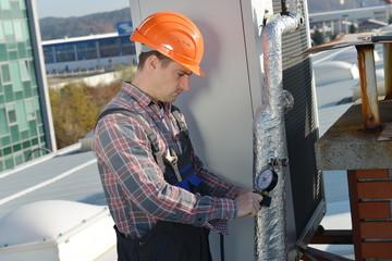 Air Conditioning Repair, young repairman on the roof fixing AC