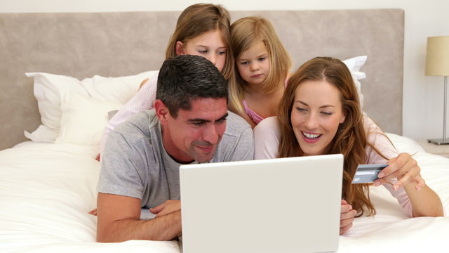 Parents and daughters lying on bed shopping online with laptop