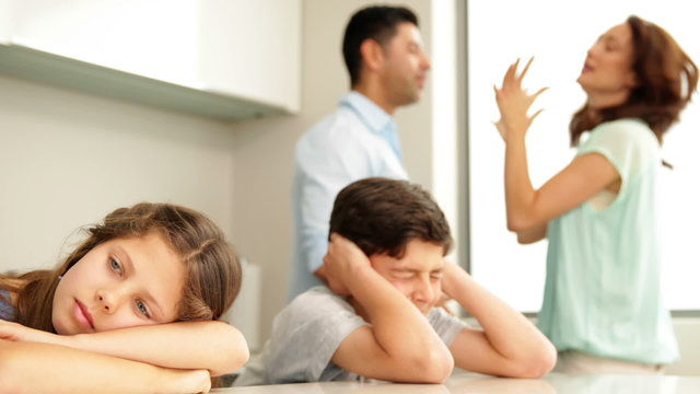 Upset siblings covering their ears while their parents fight