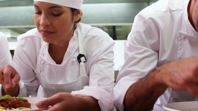 Row of chefs garnishing spaghetti dishes with basil leaf