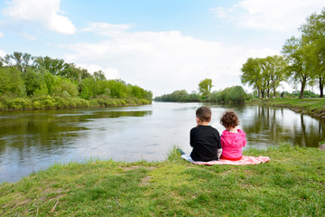 Brother and little sister sitting on the bank of the river.