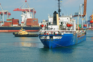 Tugboat assisting bulk cargo ship to harbor quayside