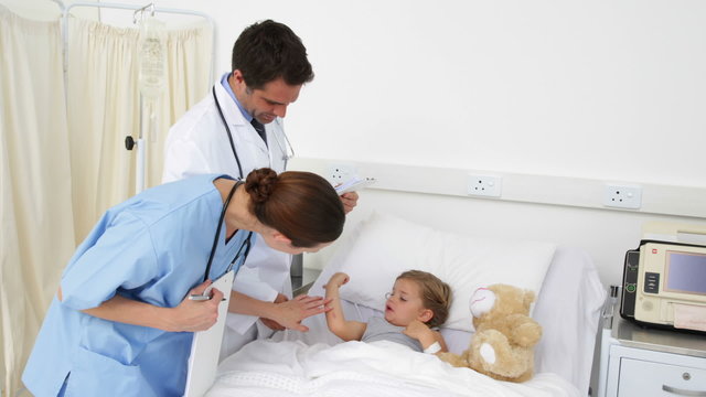 Sick little girl lying in bed talking to nurse and doctor