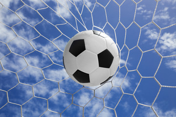 Soccer ball in goal net with blue sky