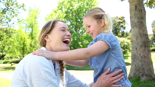 Happy little girl telling her mother a secret in the park