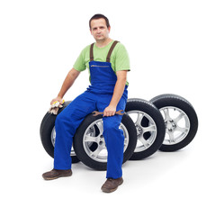 Friendly car mechanic sitting on tires