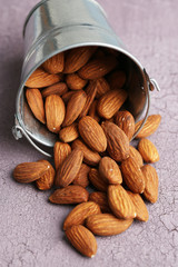 Almonds in bucket on color wooden background