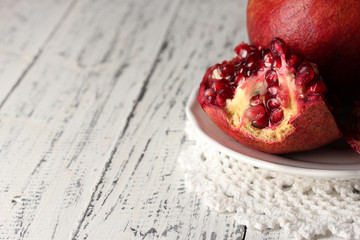Ripe pomegranates on plate, on color wooden background