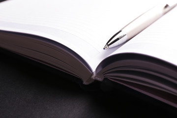 Pen on opened book on black table, close up