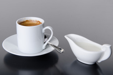 A cup of coffee with a milk jug