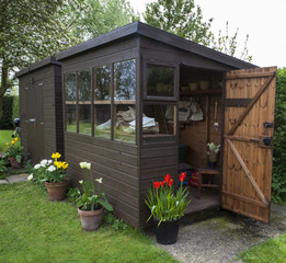 Garden shed with door open, tools, flowers, and plant pots.