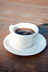 White porcelain cup of black coffee on wooden table. Outdoors