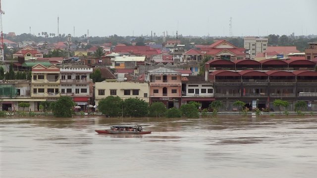 Small motorboat proceeding down the Mekong river. Riverside town protected from the rise in the water level with sandbags placed along the Mekong river ( flooded river)
