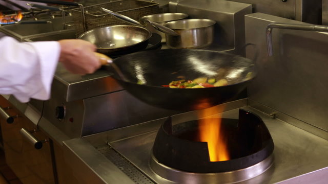 Chef tossing vegetables over a large flame