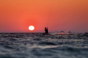 Silhouette of a kitesurfer sailing at sunset